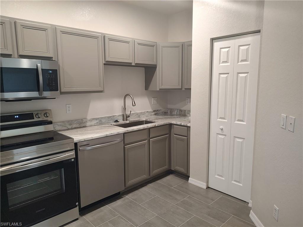 Kitchen with gray cabinetry, stainless steel appliances, and light stone counters
