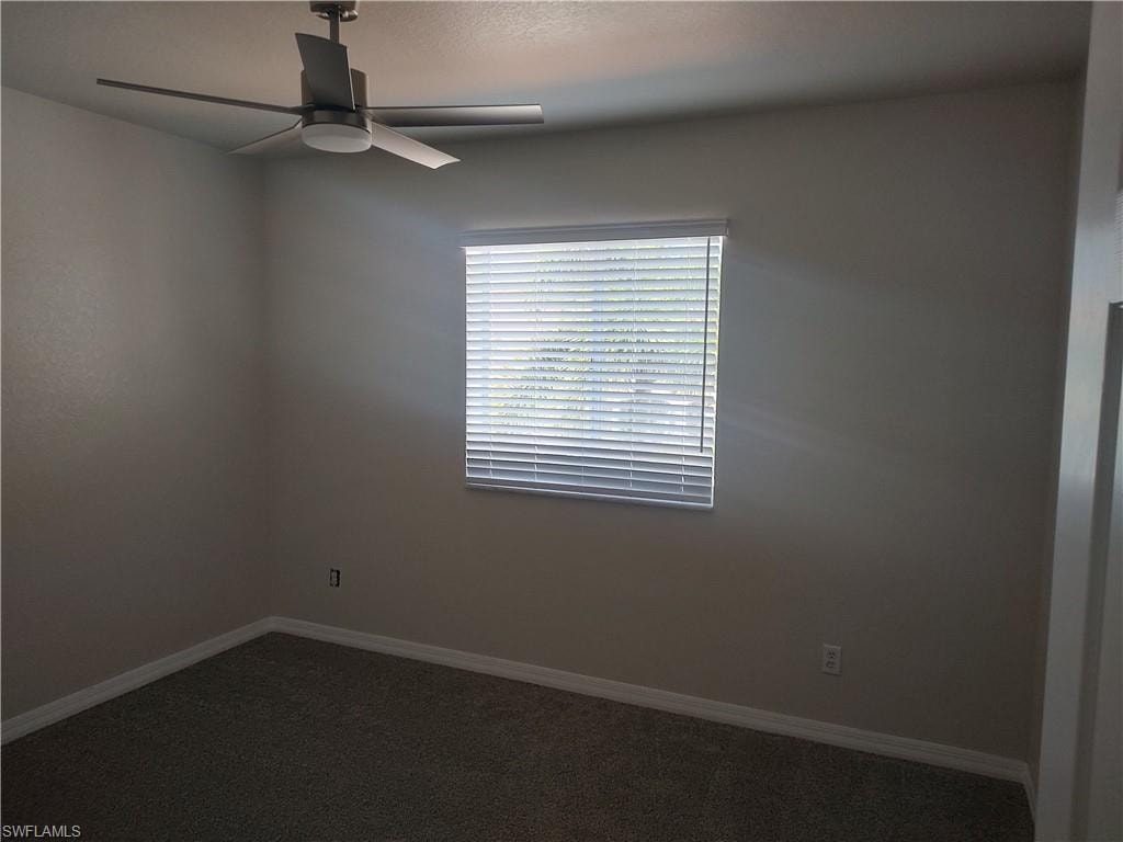 Unfurnished room with ceiling fan and dark carpet