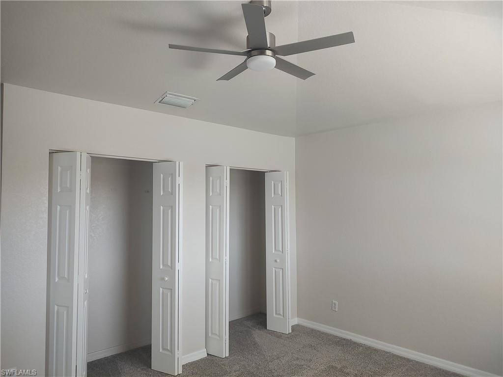Unfurnished bedroom featuring dark carpet, multiple closets, and a ceiling fan