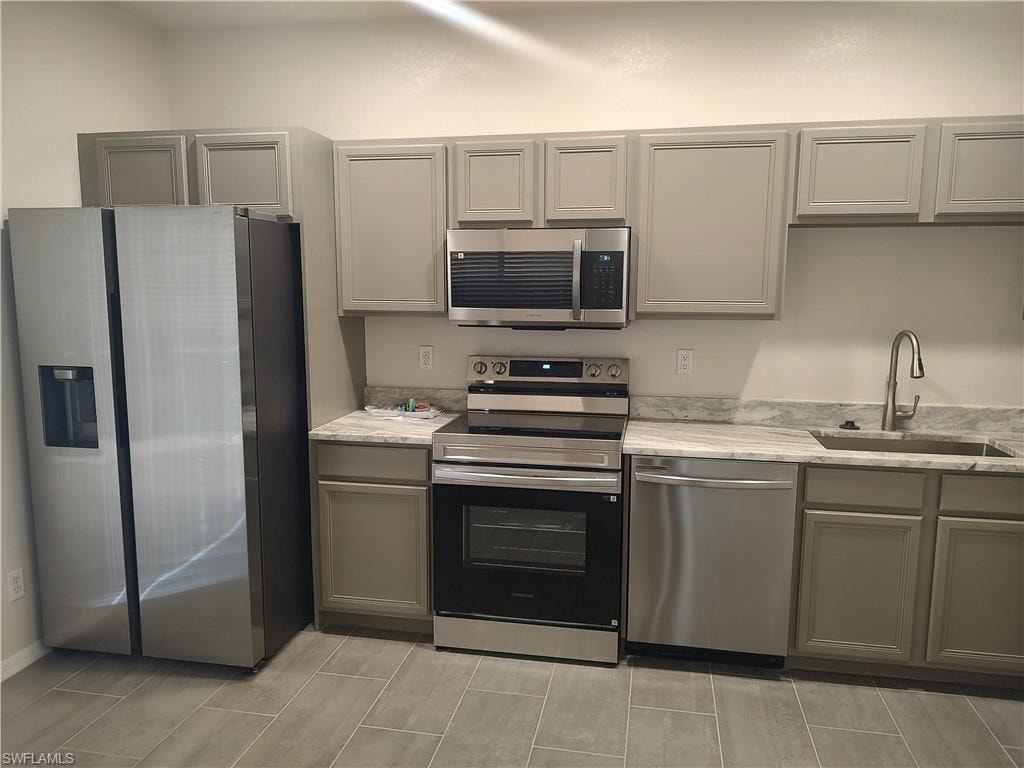 Kitchen featuring gray cabinetry, stainless steel appliances, and light stone countertops