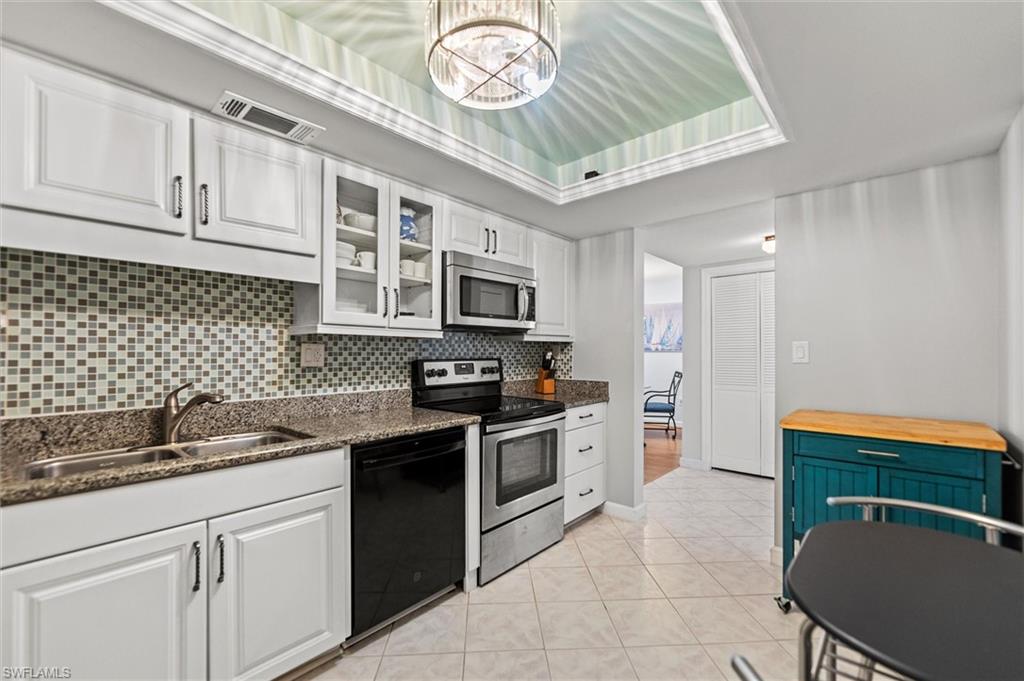 Kitchen featuring stainless steel appliances, white cabinetry, hanging lights, dark stone counters, and a tray ceiling