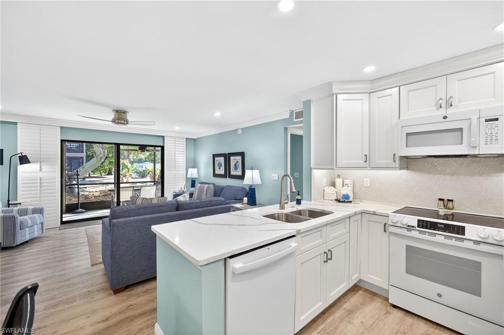 Kitchen featuring white appliances, open floor plan, light wood finished floors, ornamental molding, and light stone counters