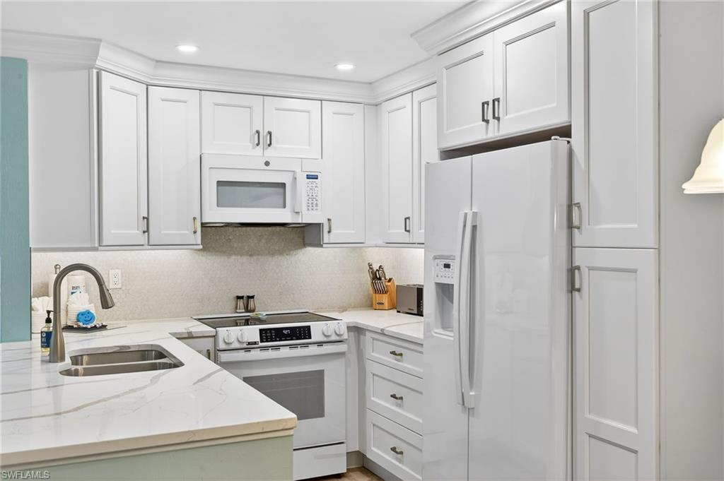 Kitchen featuring white appliances, light stone counters, white cabinets, and recessed lighting