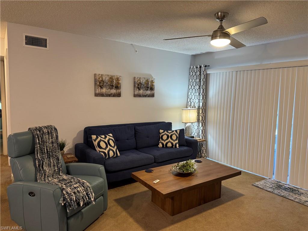 Living area featuring carpet flooring, a textured ceiling, and a ceiling fan