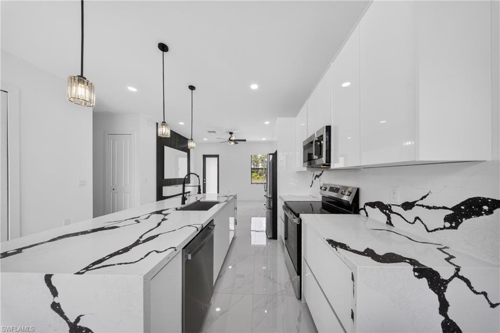 Modern kitchen featuring an expansive island with a waterfall-edge countertop, black and white veined surfaces, sleek white cabinetry, and stainless steel appliances