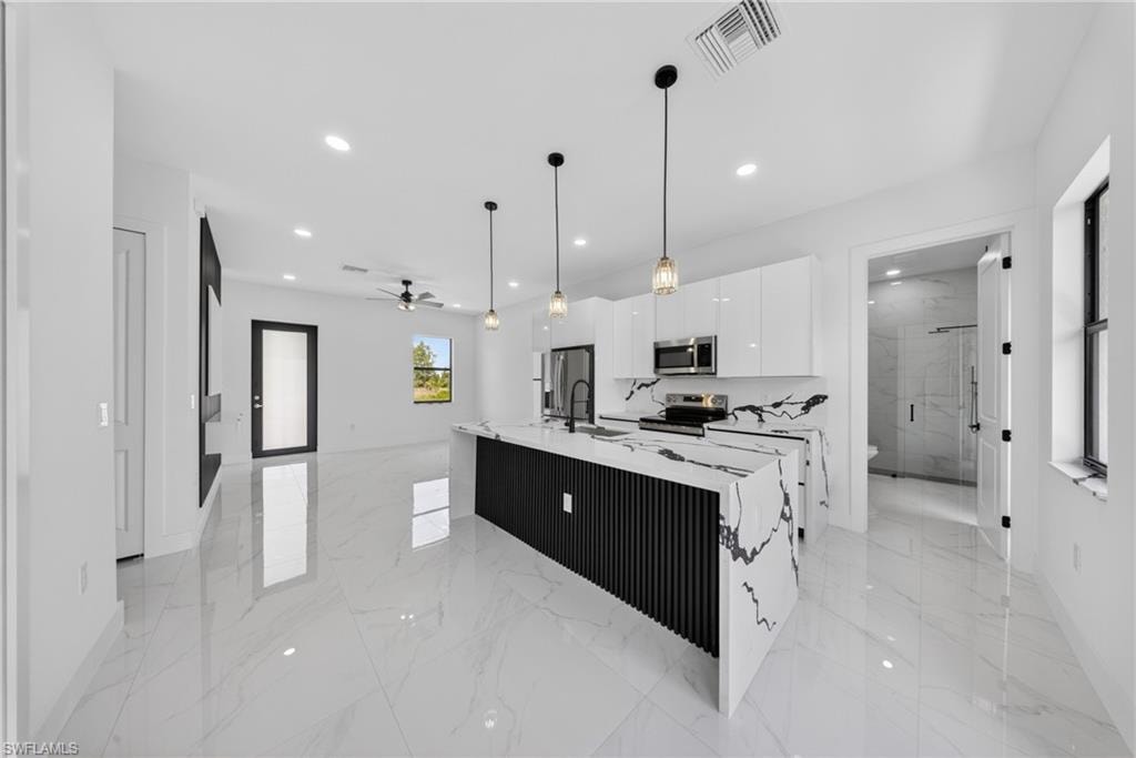 Kitchen featuring a large waterfall island with a black slatted base, white high-gloss cabinetry, integrated stainless steel appliances, pendant lighting, and polished tile flooring