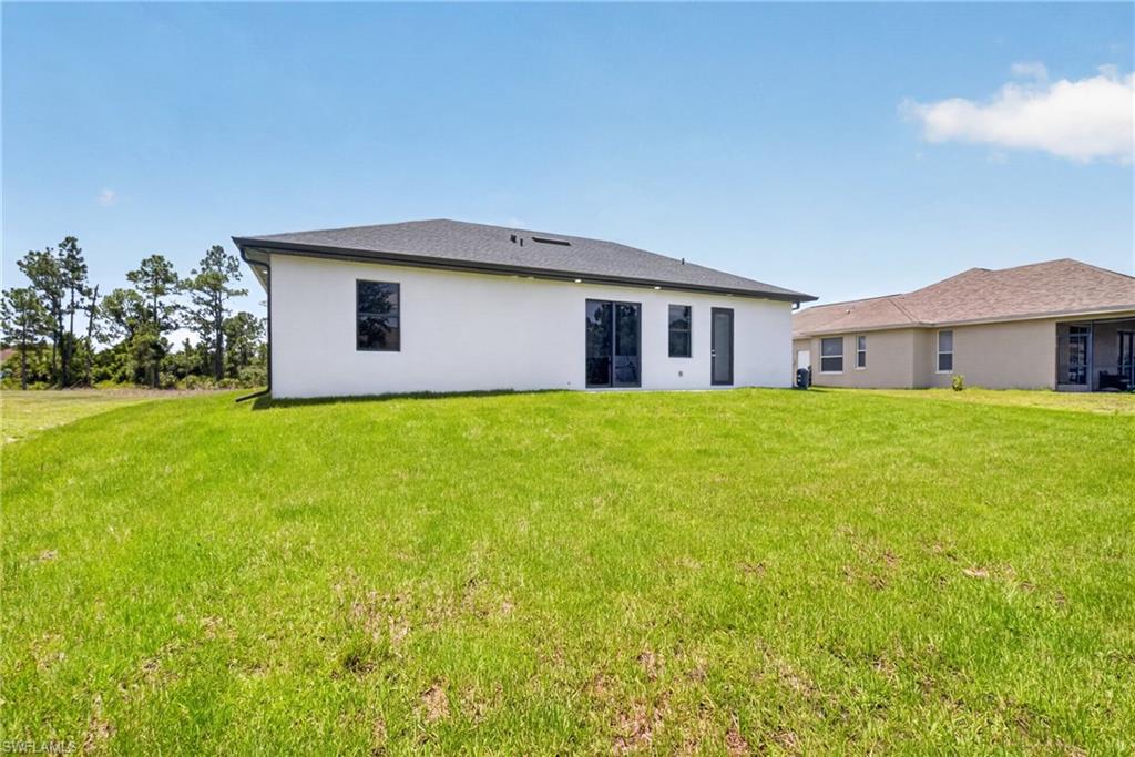 Expansive green lawn surrounds the rear of the property, featuring a white stucco exterior with a dark shingle roof