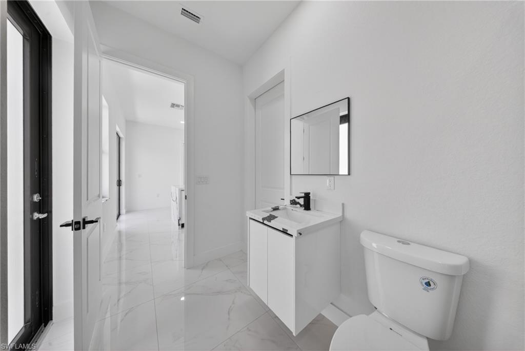 Bathroom featuring a white vanity with integrated sink, black single-handle faucet, rectangular mirror, and a white toilet
