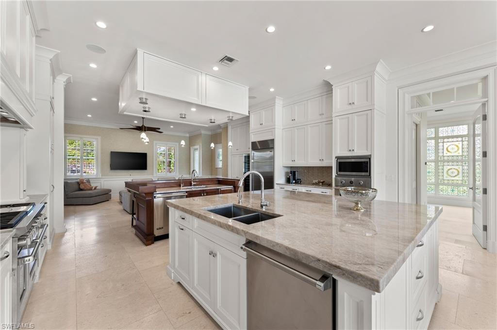 Kitchen featuring a large island, built in appliances, a sink, open floor plan, and crown molding