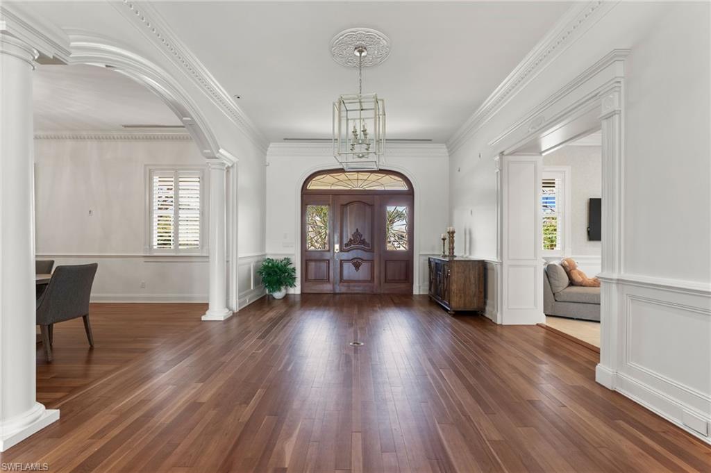 Foyer entrance with decorative columns, arched walkways, wood finished floors, and a healthy amount of sunlight