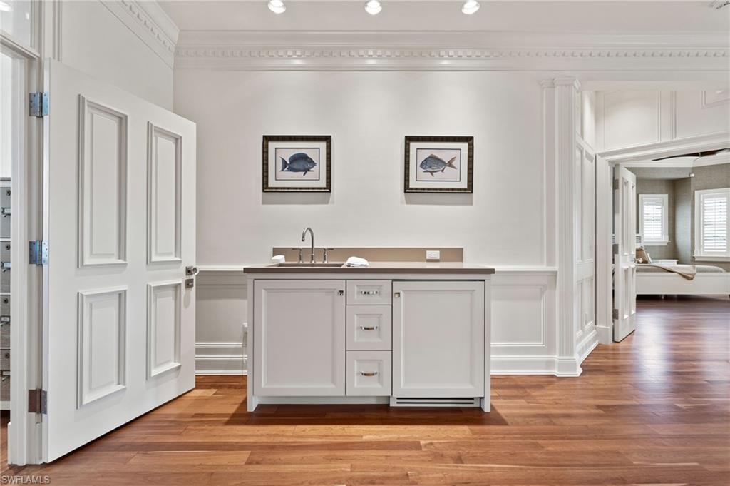 Bar featuring light wood-style floors, a decorative wall, wet bar, ornamental molding, and a sink