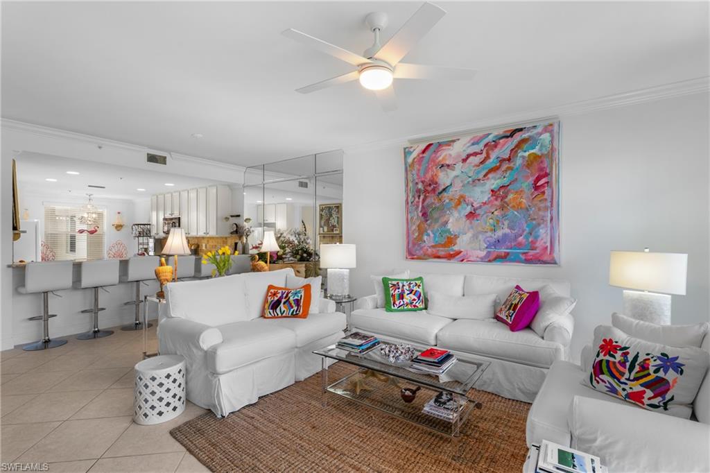 Living area with light tile patterned flooring, ceiling fan, ornamental molding, and visible vents