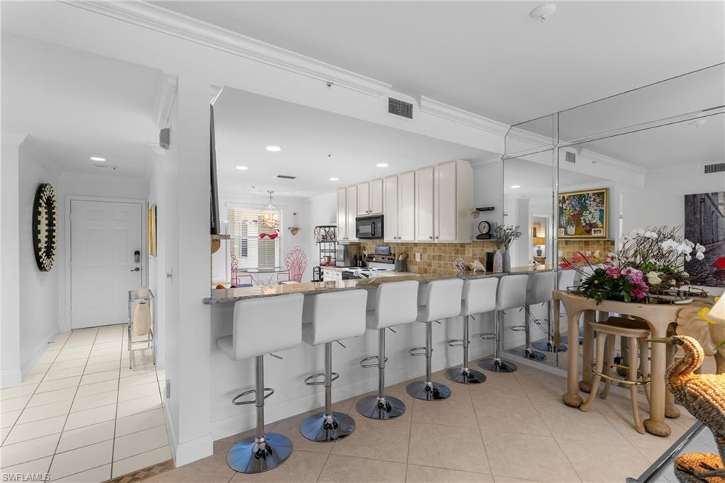 Kitchen with light tile patterned floors, range with electric stovetop, ornamental molding, black microwave, and backsplash