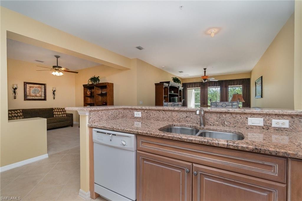Kitchen featuring light stone countertops, sink, ceiling fan, white dishwasher, and light tile patterned floors
