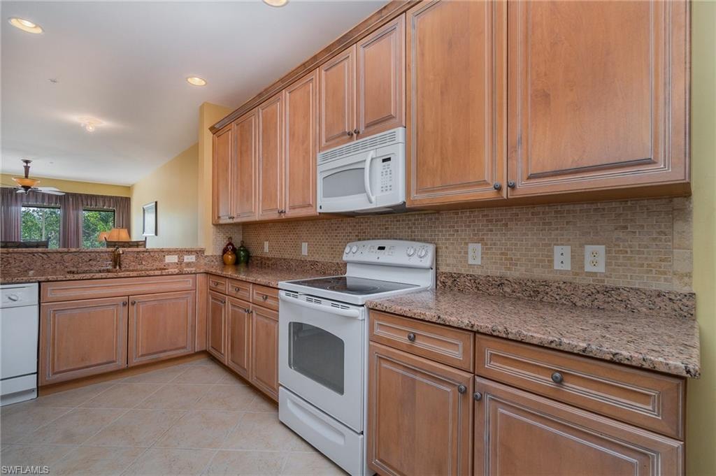Kitchen with sink, tasteful backsplash, light stone counters, white appliances, and light tile patterned floors