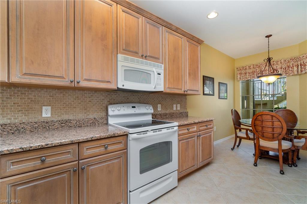 Kitchen featuring light stone countertops, tasteful backsplash, white appliances, light tile patterned floors, and hanging light fixtures