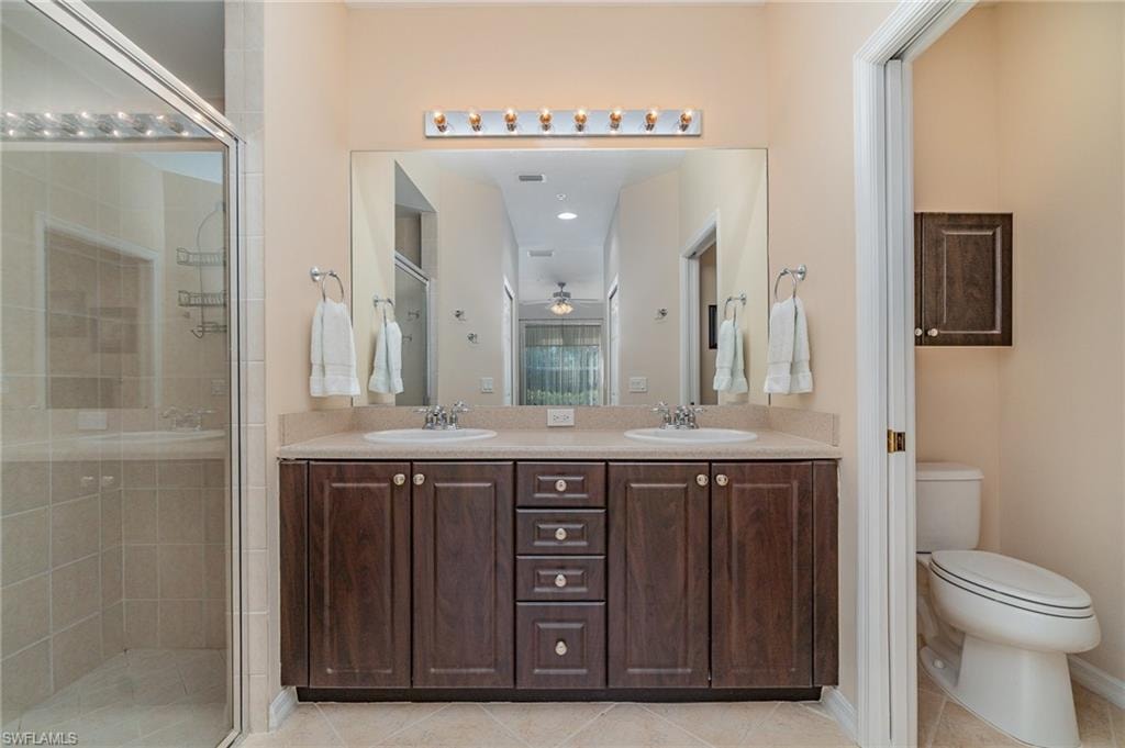 Bathroom with vanity, a shower with door, tile patterned floors, ceiling fan, and toilet