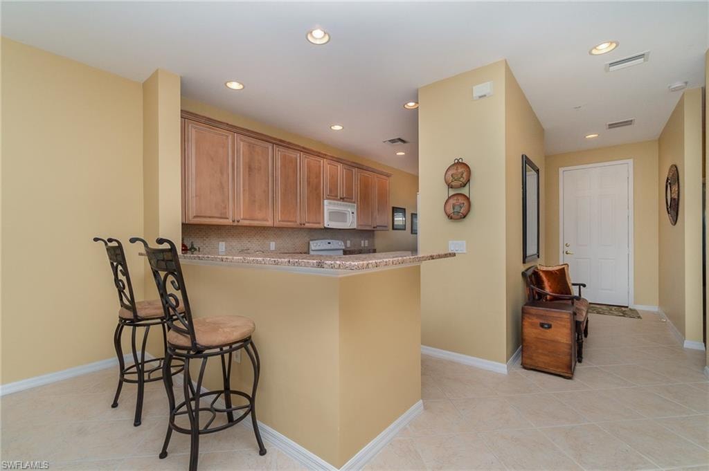 Kitchen with a kitchen bar, kitchen peninsula, backsplash, and light tile patterned flooring