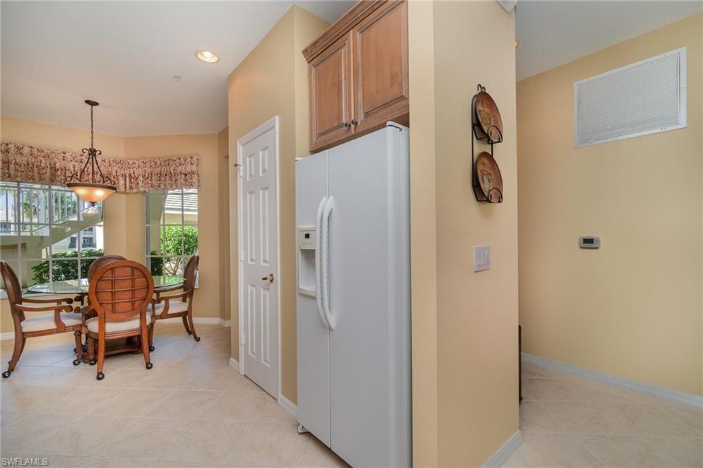 Kitchen with hanging light fixtures, white fridge with ice dispenser, and light tile patterned flooring