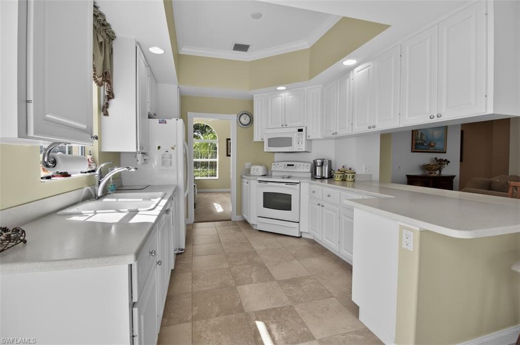 Kitchen featuring a peninsula, white cabinetry, ornamental molding, white appliances, and light countertops