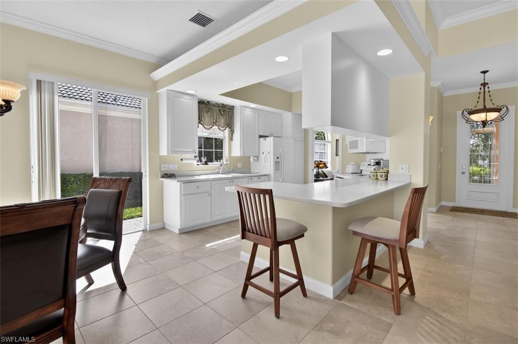 Kitchen with ornamental molding, a kitchen breakfast bar, a peninsula, light countertops, and white cabinetry
