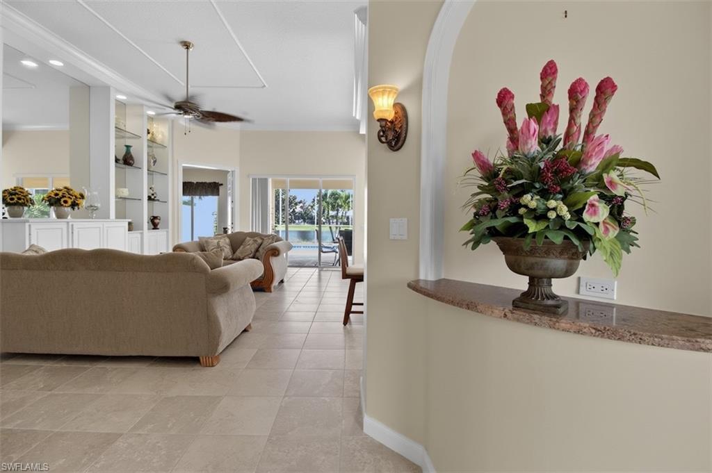 Living room featuring ceiling fan, built in features, crown molding, light tile patterned floors