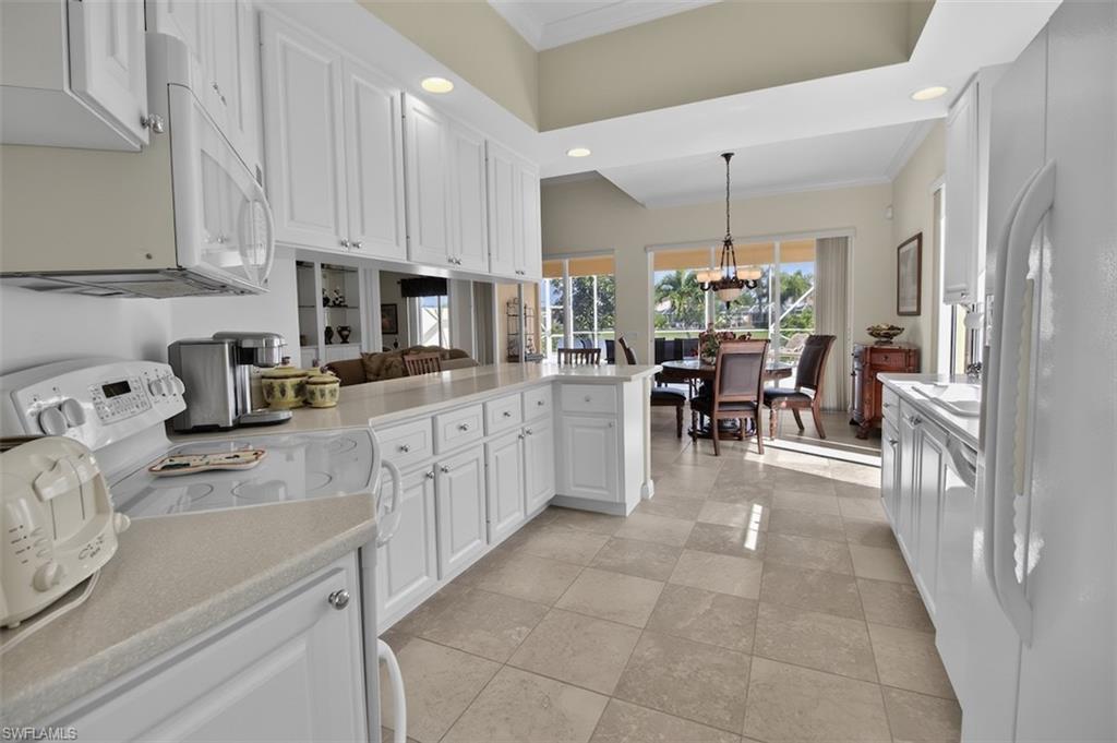 Kitchen with white appliances, ornamental molding, white cabinetry, a peninsula, and hanging lights