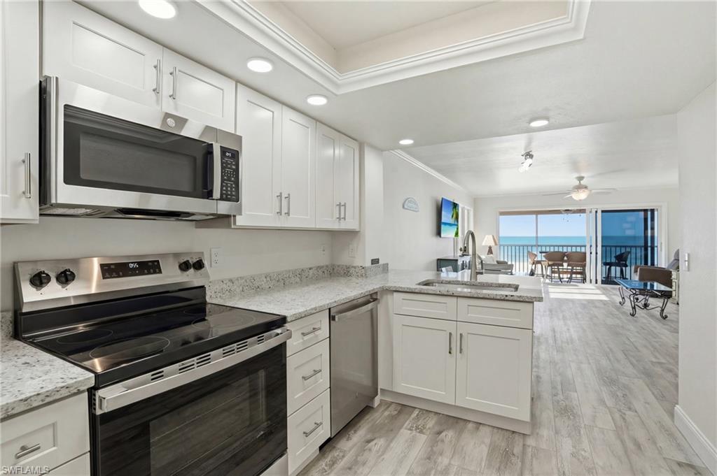 Kitchen with stainless steel appliances, open floor plan, white cabinetry, ornamental molding, and light wood-type flooring - Virtually Edited Image