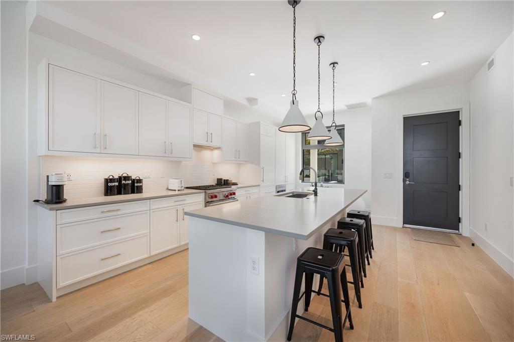 Kitchen featuring white cabinets, a breakfast bar, a large island with sink, and light wood finished floors