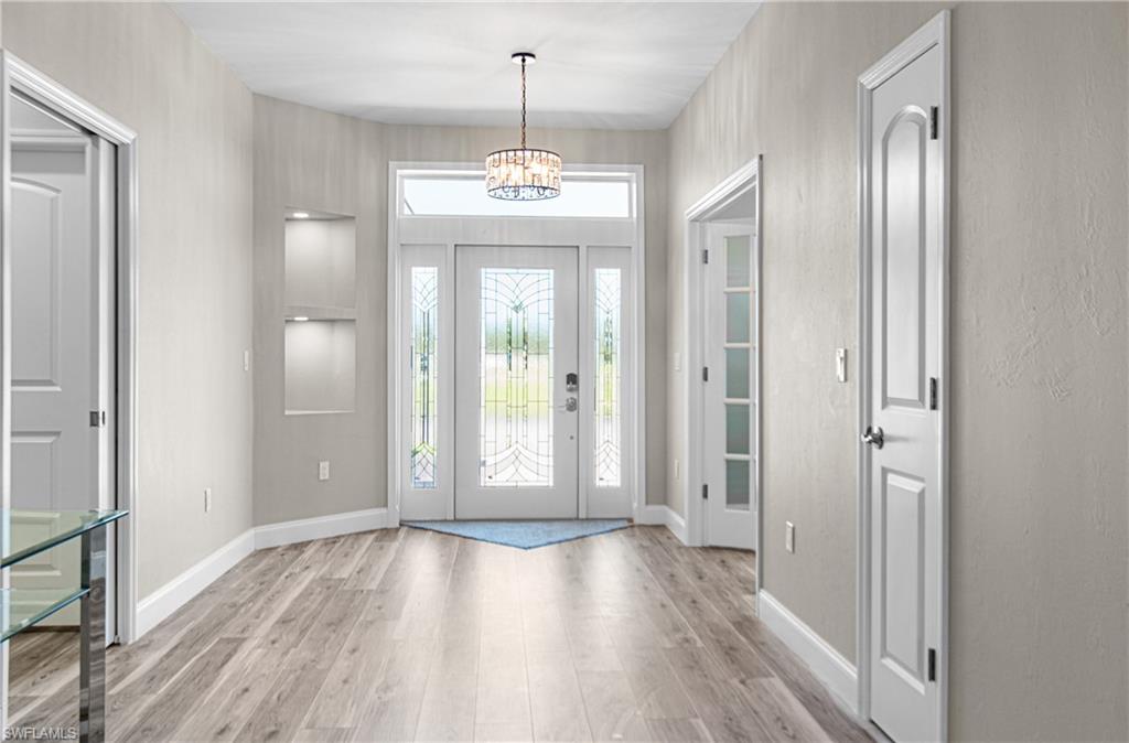 THE ENTRY HALL IS A STATEMENT IN ITSELF WITH LIGHTED RECESSED DECORATIVE SHELF, SPARKLING CHANDELIER, AND GLASS DOOR