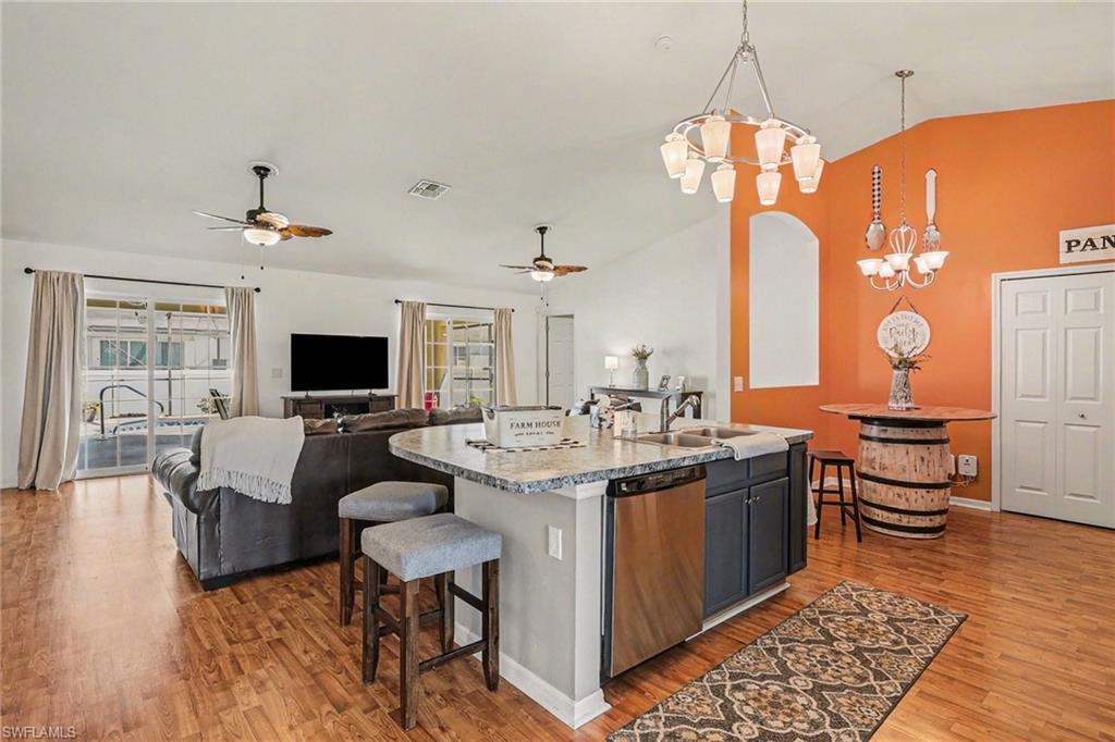 Kitchen featuring open floor plan, dishwasher, a center island with sink, light wood-type flooring, and vaulted ceiling