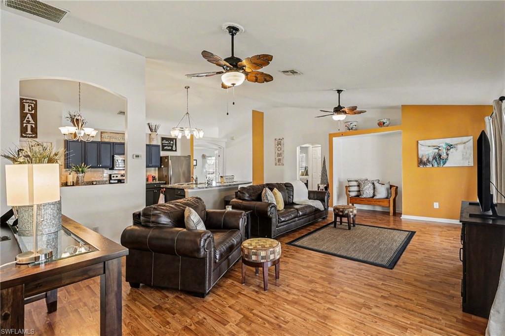 Living room featuring suspended lighting, wood finished floors, vaulted ceiling, ceiling fan, and arched walkways