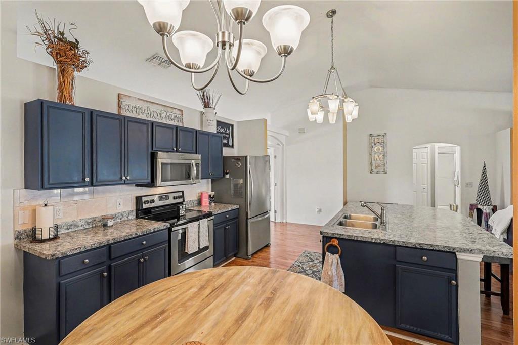 Kitchen with stainless steel appliances, arched walkways, light wood-type flooring, an island with sink, and suspended lighting