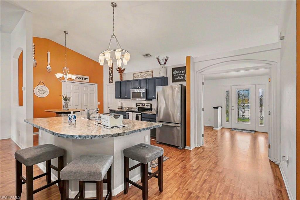Kitchen featuring a kitchen breakfast bar, stainless steel appliances, arched walkways, light wood-style flooring, and lofted ceiling