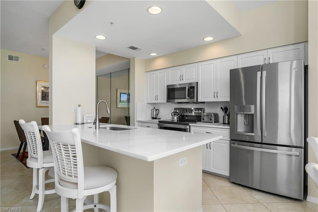 Kitchen with light tile patterned flooring, a sink, stainless steel appliances, a kitchen bar, and visible vents