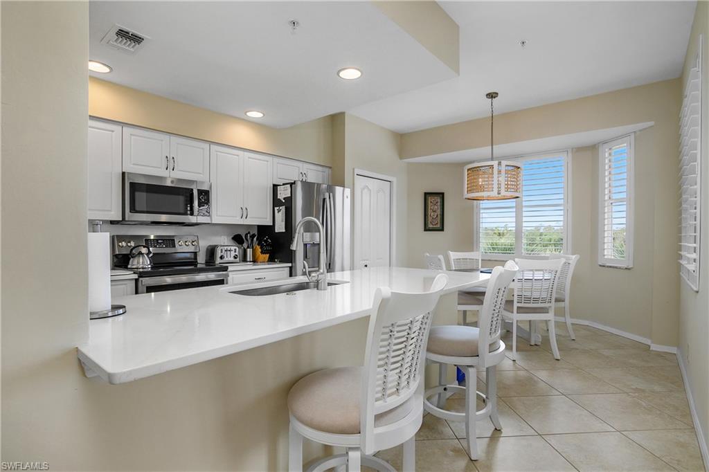 Kitchen featuring visible vents, a breakfast bar, a sink, appliances with stainless steel finishes, and decorative light fixtures