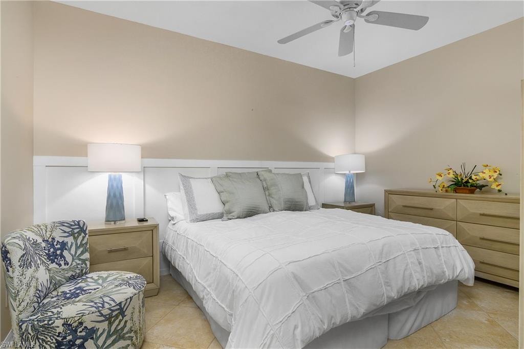 Bedroom featuring light tile patterned floors, a wainscoted wall, and ceiling fan
