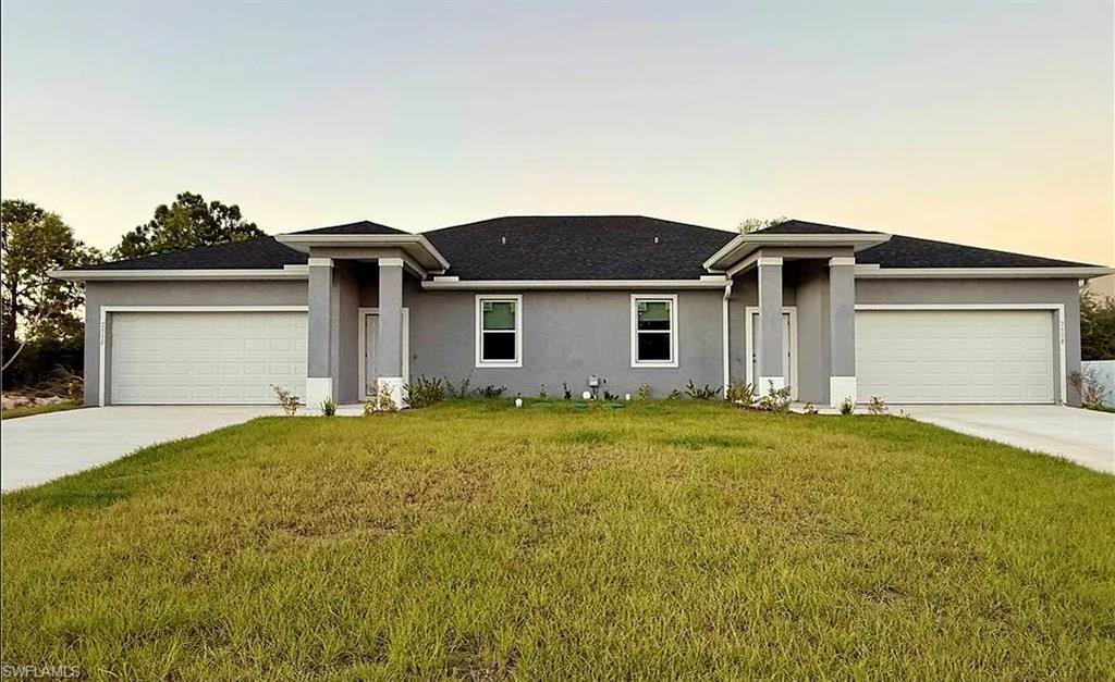 View of front of property with a garage, a lawn, stucco siding, and driveway