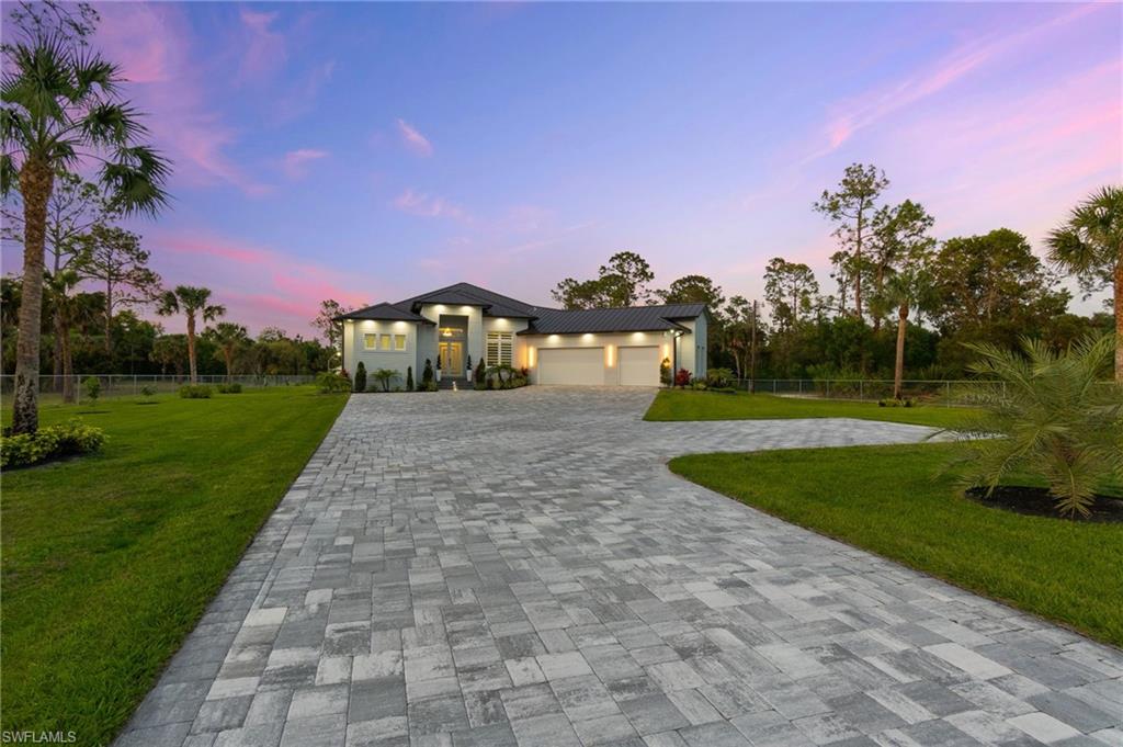 View of front facade featuring decorative driveway, a yard, fence, and an attached garage