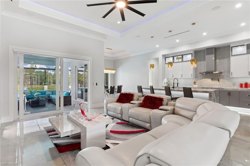 Living room with a raised ceiling, ornamental molding, a ceiling fan, recessed lighting, and baseboards