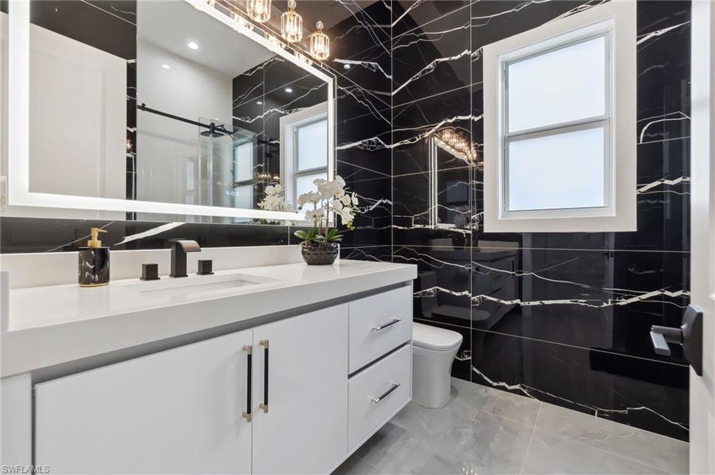 Bathroom with vanity, tile walls, toilet, and a wealth of natural light