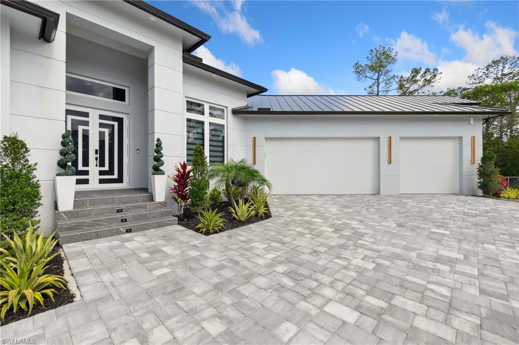 Entrance to property featuring decorative driveway, metal roof, a garage, and stucco siding