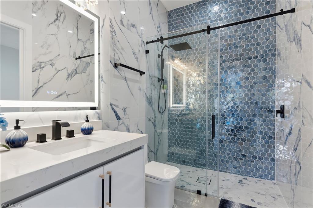 Bathroom featuring toilet, a stall shower, tile walls, and vanity