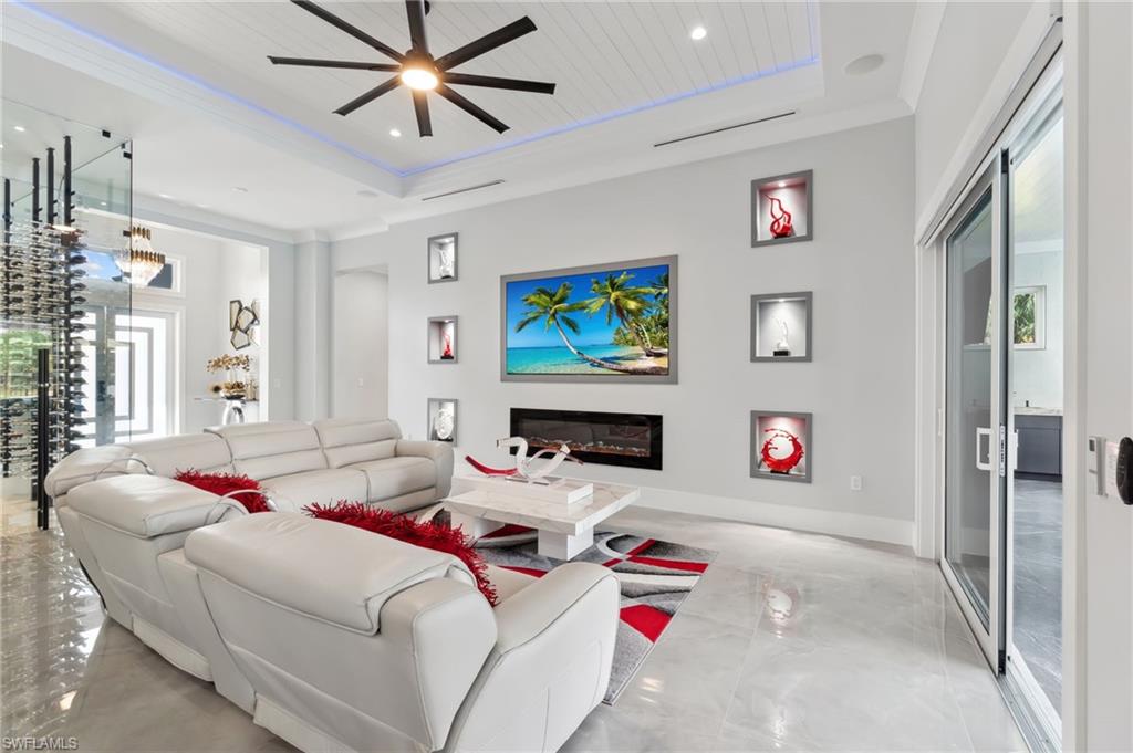 Living area featuring ceiling fan, baseboards, a tray ceiling, recessed lighting, and a glass covered fireplace