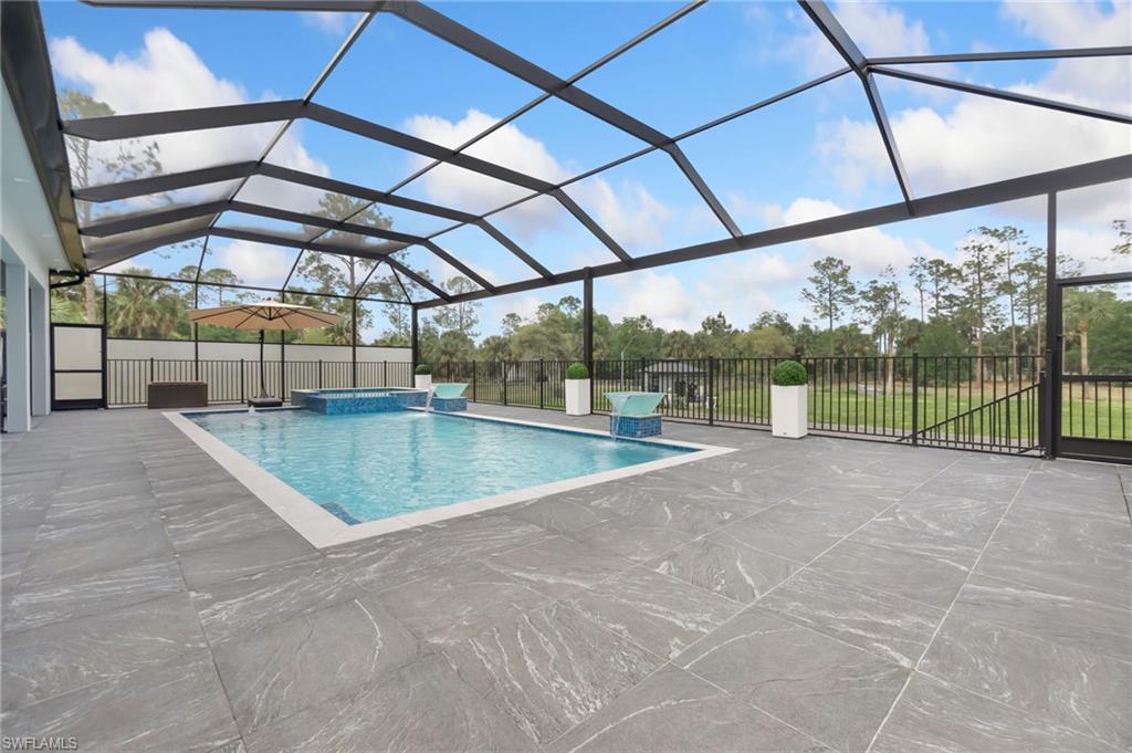 View of pool with a patio, fence, a lanai, and a pool with connected hot tub