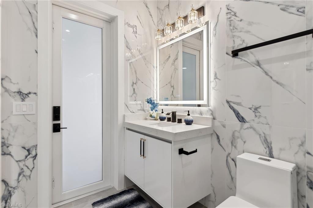 Bathroom with tile walls, toilet, stone wall, and vanity