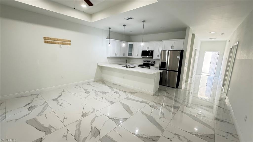 Kitchen featuring stainless steel appliances, white cabinetry, hanging light fixtures, glass insert cabinets, and a peninsula