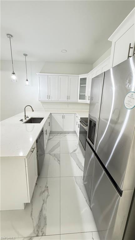 Kitchen featuring white cabinetry, stainless steel appliances, pendant lighting, a peninsula, and glass fronted cabinets