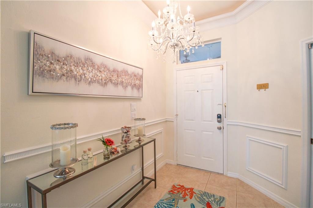 Entryway featuring ornamental molding, light tile floors, and an inviting chandelier