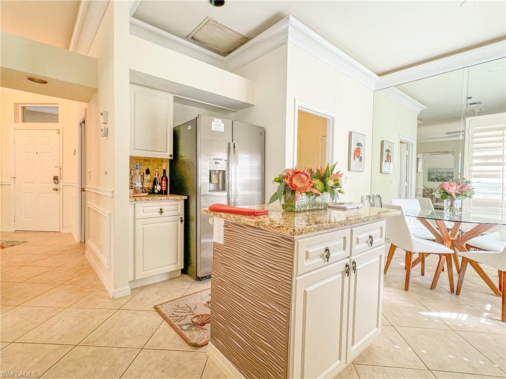 Kitchen with light stone counters, stainless steel fridge with ice dispenser, light tile floors, and tasteful backsplash